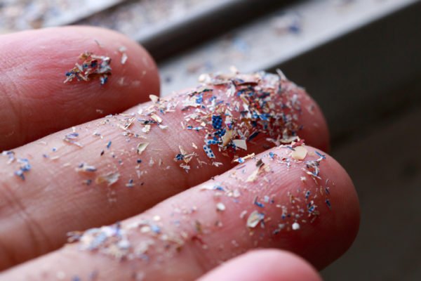 Close-up shot of tiny, coloured microplastic particles like dust on human fingertips