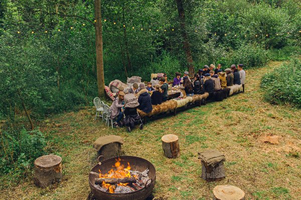Friends and family sharing food at a long table in the woods at Broughton Sanctuary