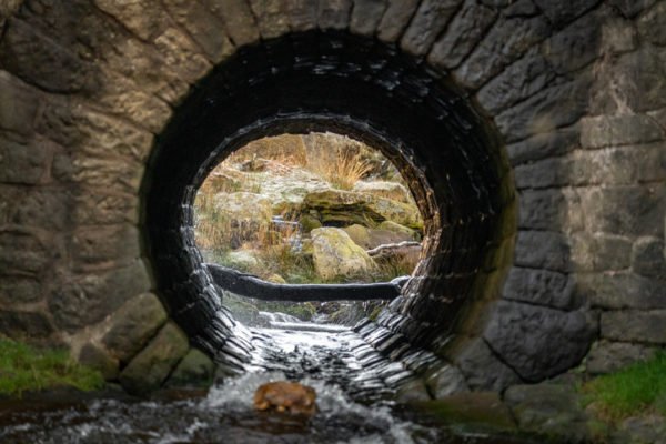 Old circular sewer brick culvert tunnel water river running through flowing, granite stone in Peak District countryside