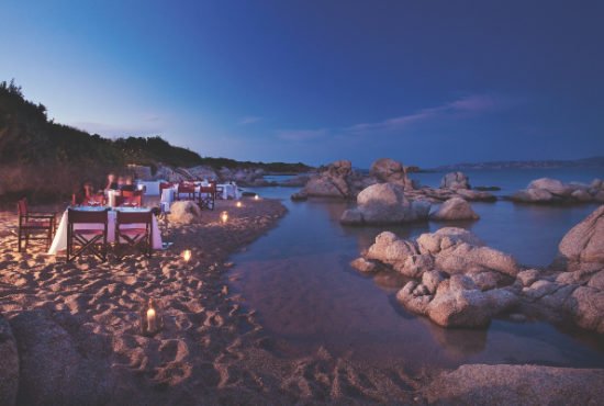 Tables set for a romantic sunset meal on a sandy beach in North Sardinia