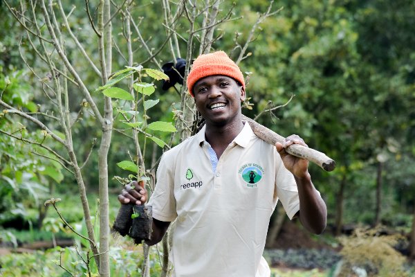 A Treepp tree-planting partner in Tanzania, smiling with spade and sapling