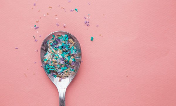 A spoon full of tiny Microplastics particles, viewed from above against a pink background