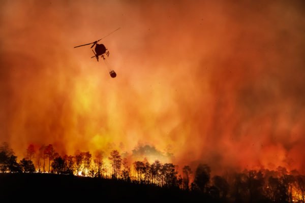 Firefighting helicopter carrying water in bucket to extinguish a forest fire