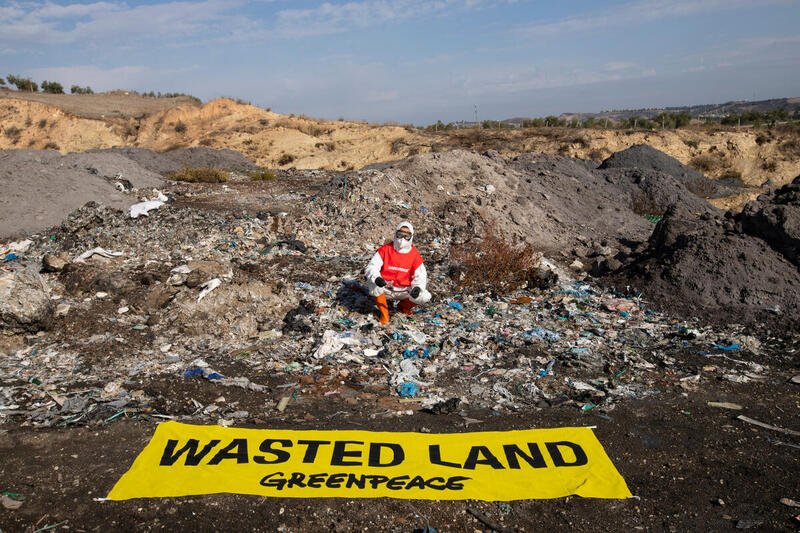 A Greenpeace campaigner sits behind a banner saying 'Wasted Land' and investigates a waste pile in Adana/Seyhan, Turkey.