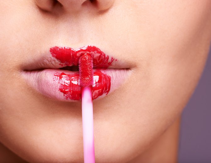 Closeup shot of a woman applying red lipgloss