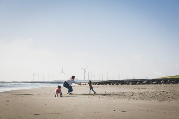 Family plays on the beach with wind farm in the background