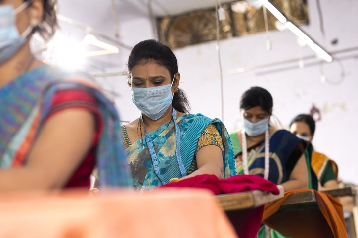 Female Indian textile workers sewing clothes with protective face mask on production line