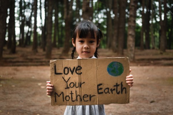 Little girl with banner protesting over pollution and global warming in the forest to save planet Earth