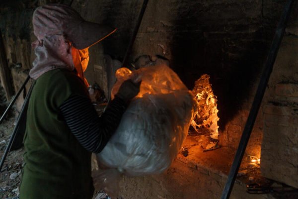 A woman loads garment offcuts into a brick kiln located in Kandal Province, Cambodia