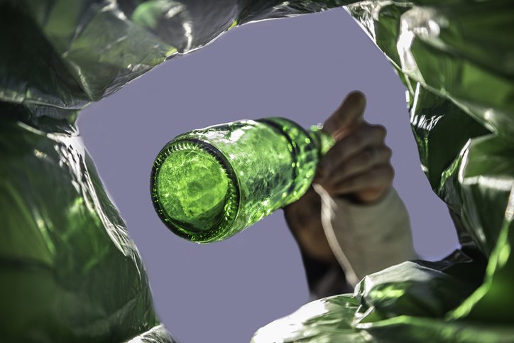 Woman recycles beer bottle in green container for glass