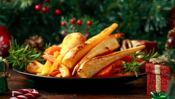 Christmas roasted parsnips and carrots with decoration, gifts, green tree branch on wooden rustic table