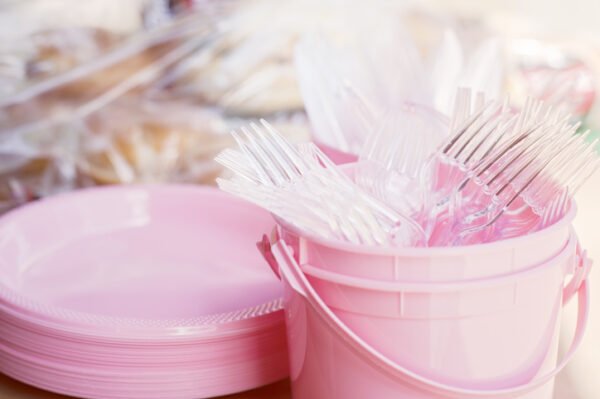 A stack of pink plates and a pink bucket filled with forks and knives made from single-use plastic