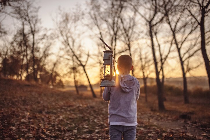 Boy standing in the woods and holding old lamp on a stick