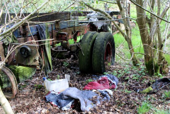 Abandoned derelict lorry in wooded field, once home to a rough sleeper. Various items of clothing can be seen around the rusty vehicle