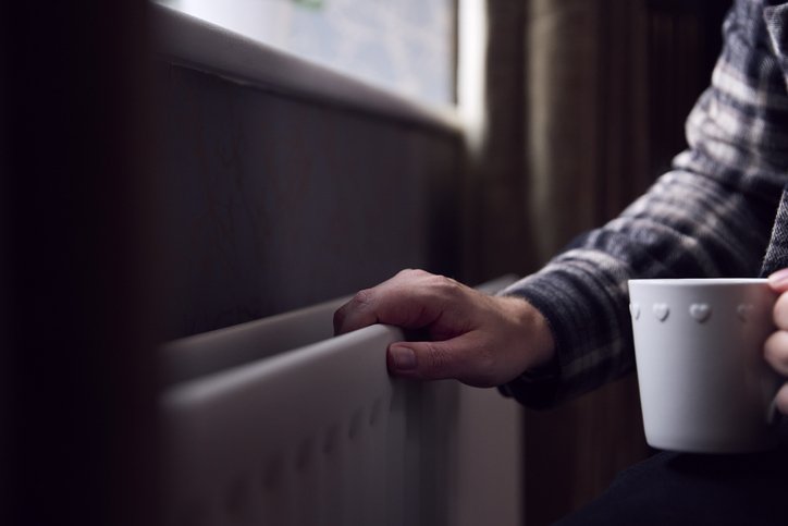 Close-up of mature man's hand on a radiator as he tries to keep warm during a cost of living crisis