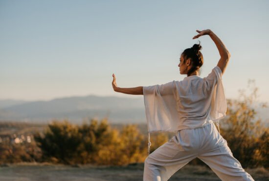 Woman doing tai chi in a meadow at sunset