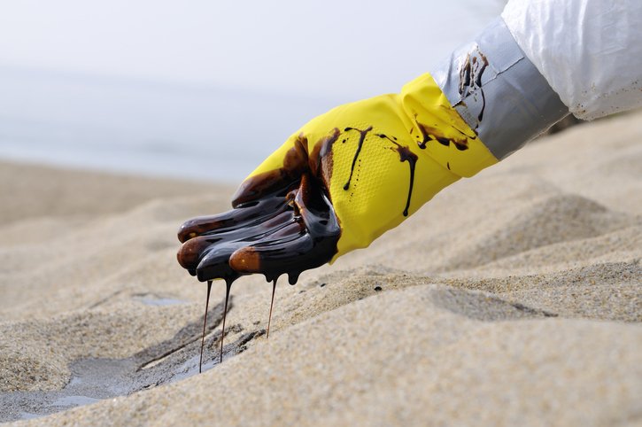 A gloved hand of unidentifiable/unnamed emergency worker scooping oil from pristine beach sand.
