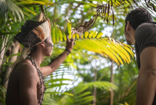 Indigenous young Brazilian man from Guarani showing the rainforest to a tourist