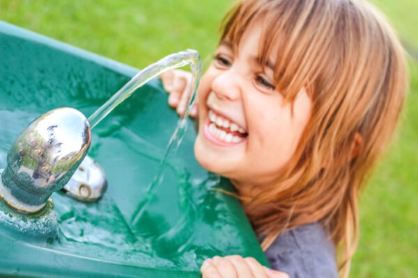 Cute and happy little girl getting water from a water fountain
