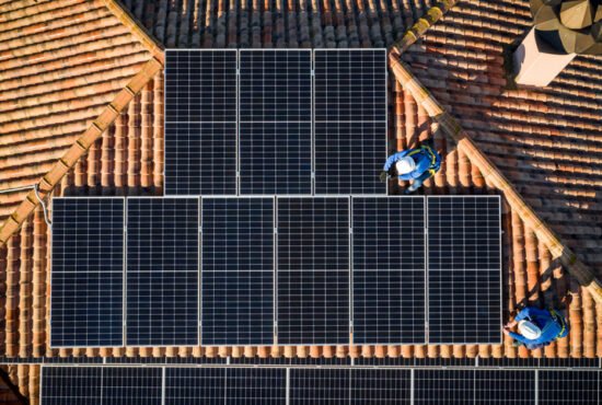 Aerial view of two workers installing solar panels on a house roof