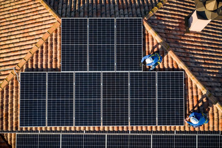 Aerial view of two workers installing solar panels on a house roof
