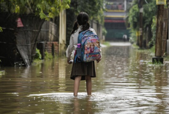 A girl returns from school wades across a flooded street after heavy rains, in Guwahati, India
