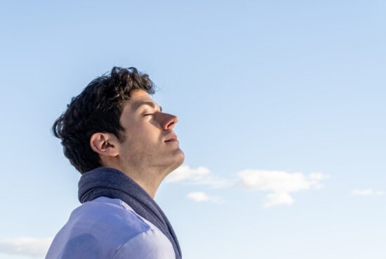 Young curly haired boy isolated on background of clear sky and with closed eyes smelling blue sky.