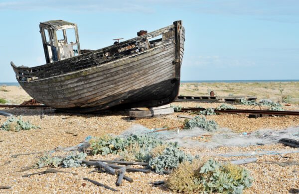 An old wooden fishing boat rotting away after years of neglect on Dungeness Beach in Kent, UK