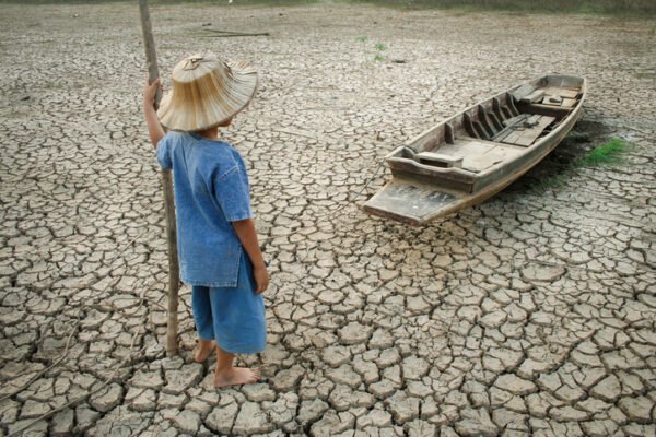 Children standing near the wooden boat on cracked earth