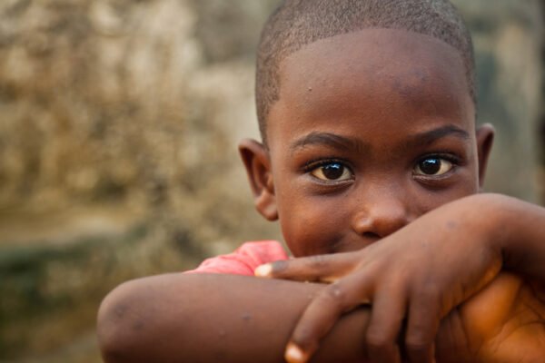 A cute African boy leaning on his elbows and smiling at the camera.