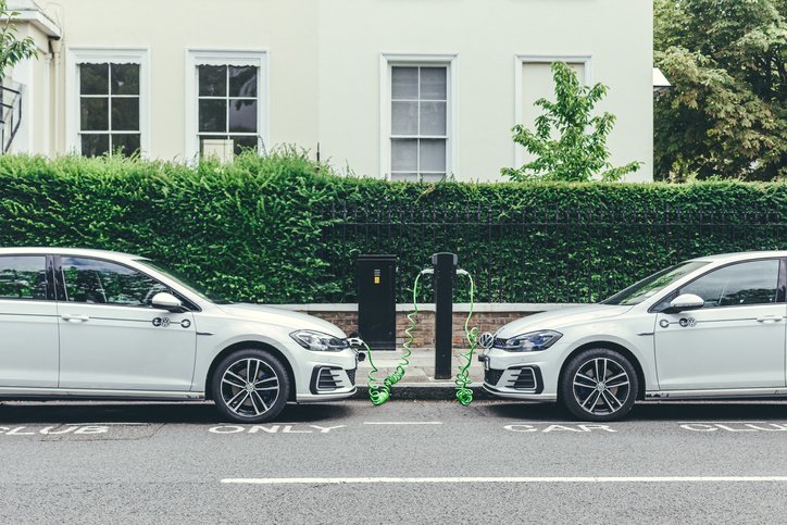 Two white Volkswagen Golf GTE cars charging at a charging point on a street in London