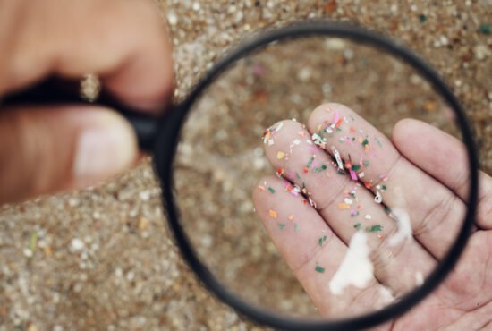 Looking through a magnifying glass at microplastics mixed with sand in a hand