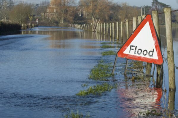 A flood warning sign, on a closed country road next to water-logged fields in the Avon Valley, Hampshire, England