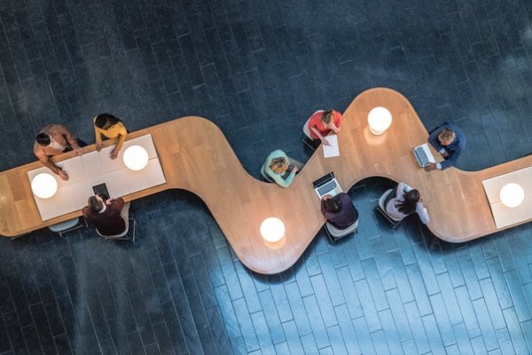 Panoramic overhead view of several business meetings going on in the communal area of a modern office building