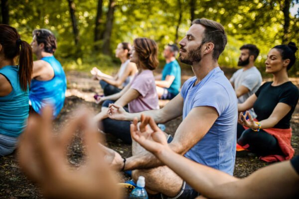 Group of Zen-like people sitting in Lotus position while exercising Yoga with their eyes closed in the park