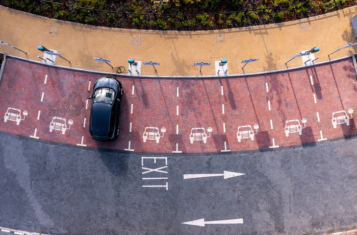 An aerial view directly above an electric vehicle charging station with electric car charging in a parking space