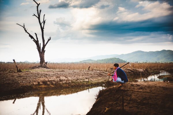 Hopeless and lonely farmer sit on cracked earth near drying water.
