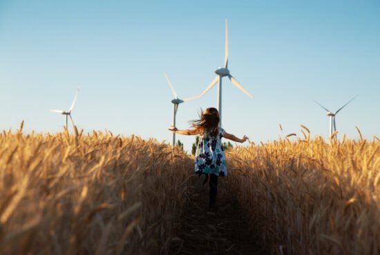 Girl running through a field to a wind turbine