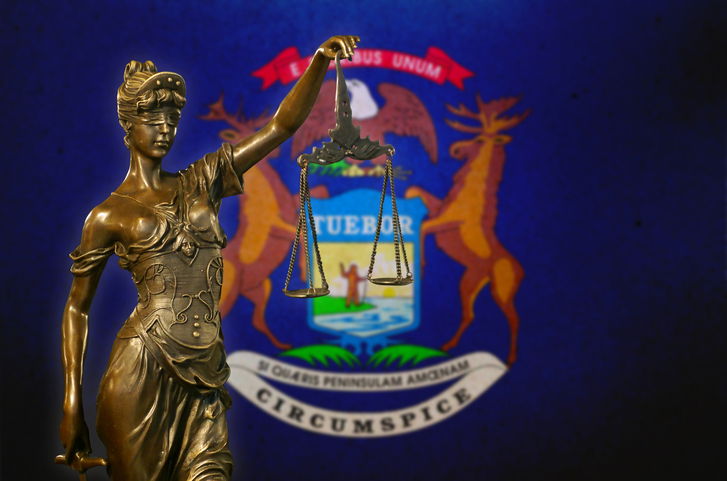 Close-up of a small bronze statuette of Lady Justice before a flag of Michigan