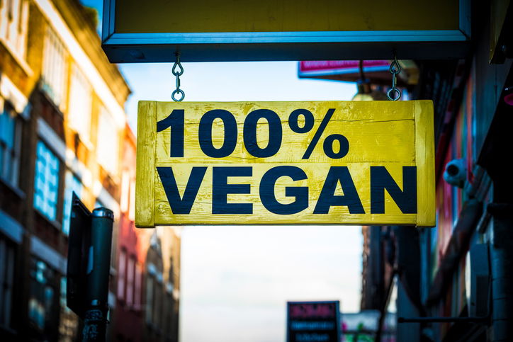 Close up colour image of a yellow sign on a city street in London, UK, saying in bold black lettering, 100% vegan