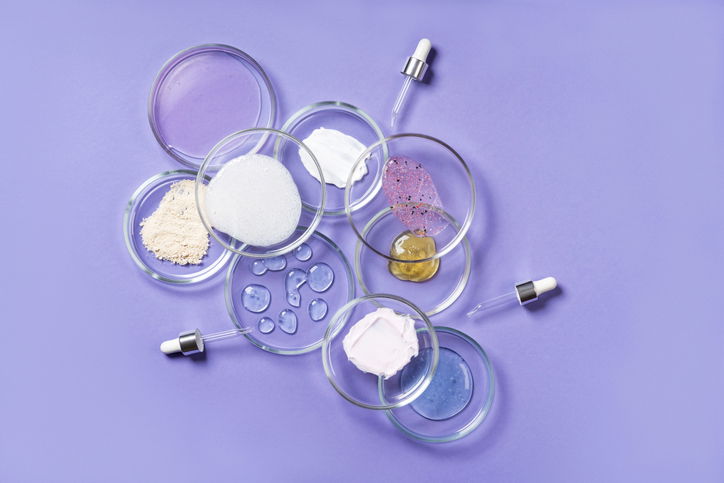Cosmetic products, scrub, face serum and gel in many petri dishes on a pink background