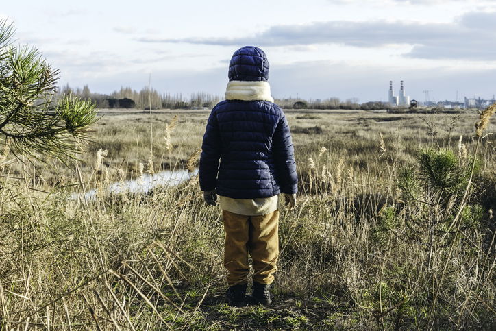 Back view of a child wearing winter clothes standing in front of wild landscape and factories