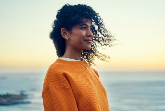 Happy woman at the beach for the sunset or sunrise in summer smiling and thinking of nature, travel and freedom