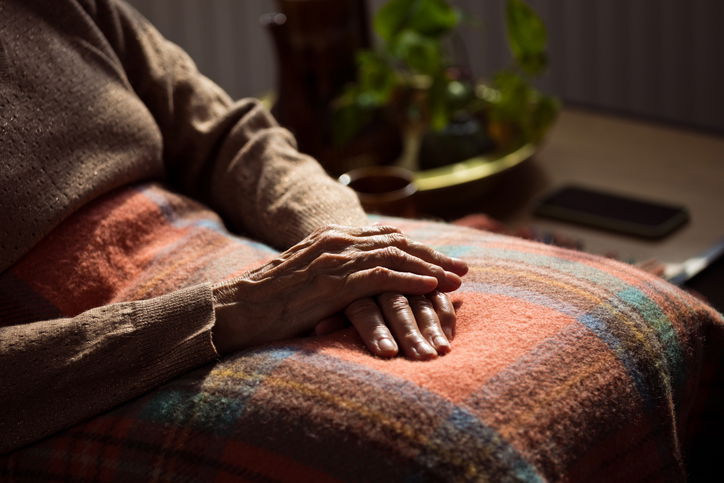 Senior woman sitting in armchair at home with legs covered by blanket