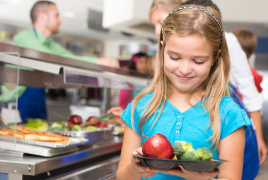 Happy little girl making healthy choices in school cafeteria.