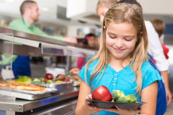 Happy little girl making healthy choices in school cafeteria.